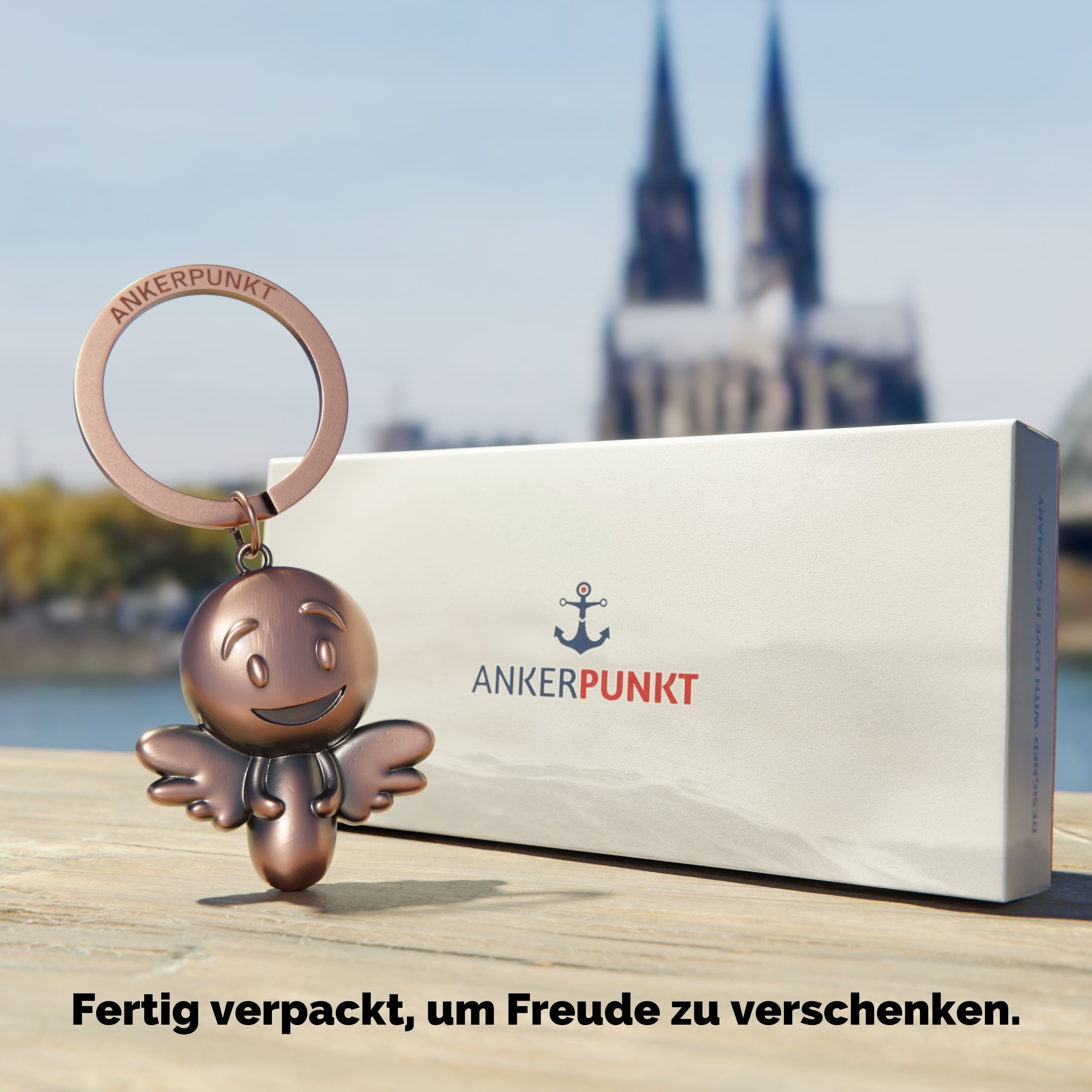 Schlüsselanhänger Engel bronze vintage mit Verpackung am Rhein, im Hintergrund ist der Kölner Dom zu sehen