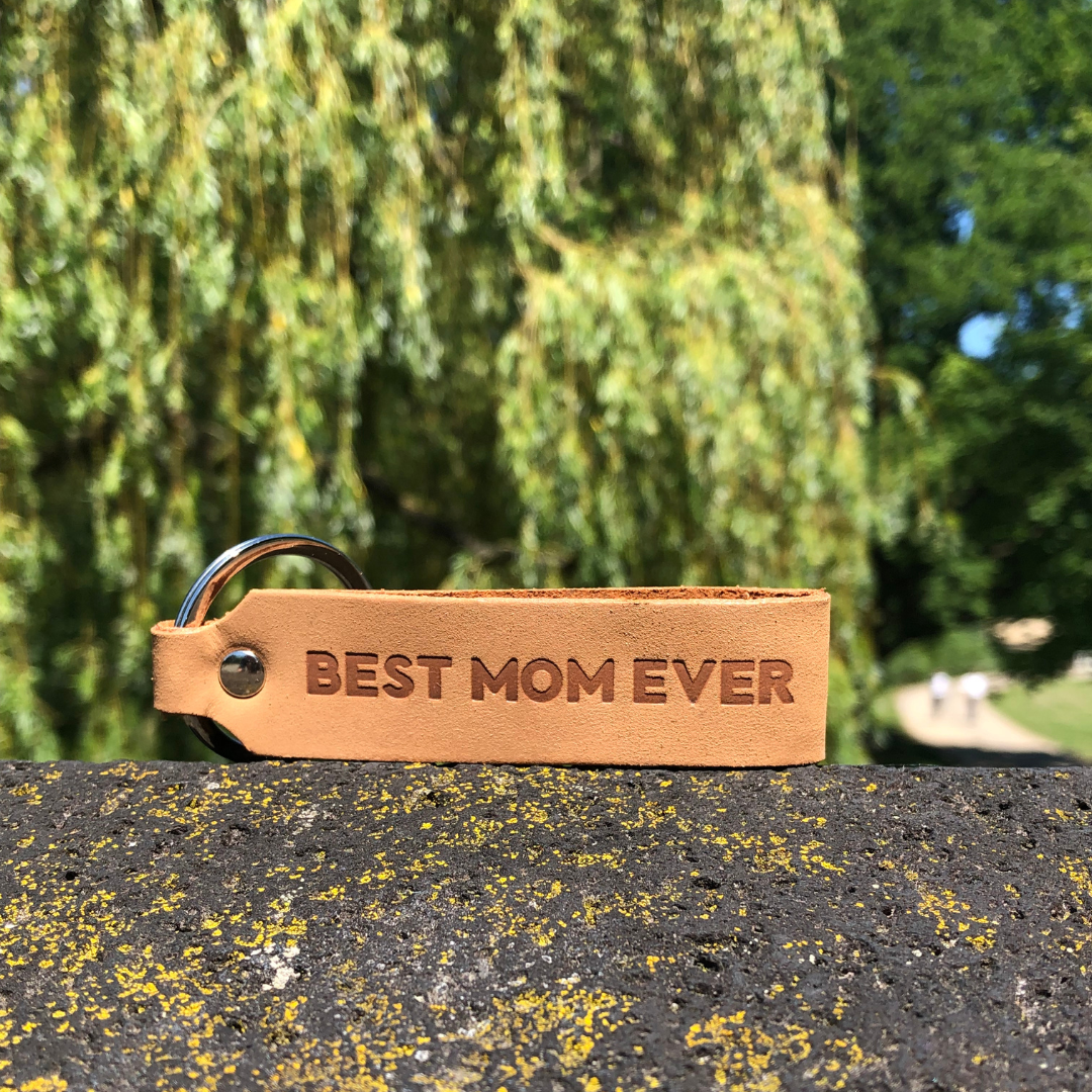 Ankerpunkt Schlüsselanhänger aus Leder mit Gravur  Best Mom Ever hellbraun liegt auf Stein im Park