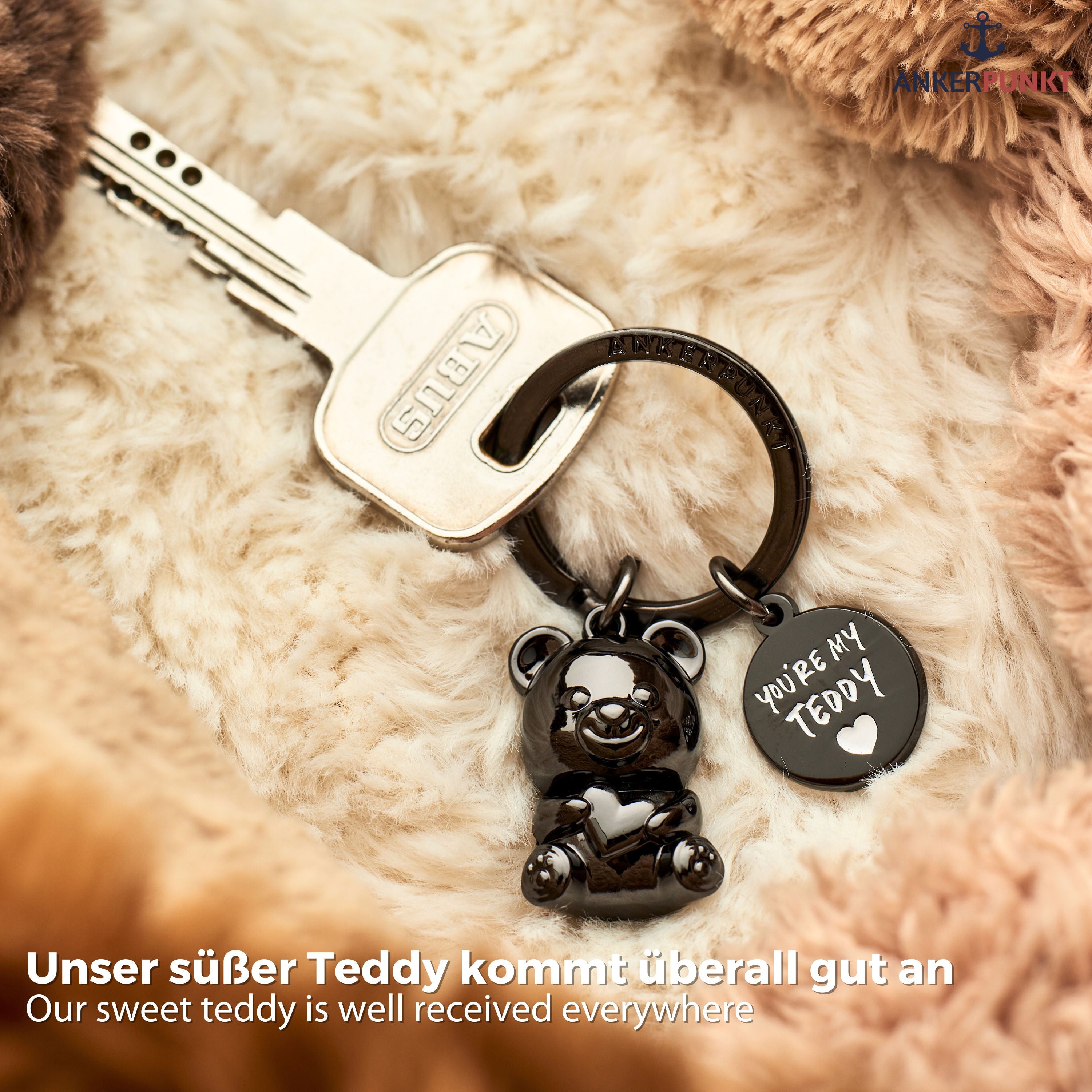 Teddybär Schlüsselanhänger in schwarz glänzend auf Tisch, daneben Laptop und Smartphone