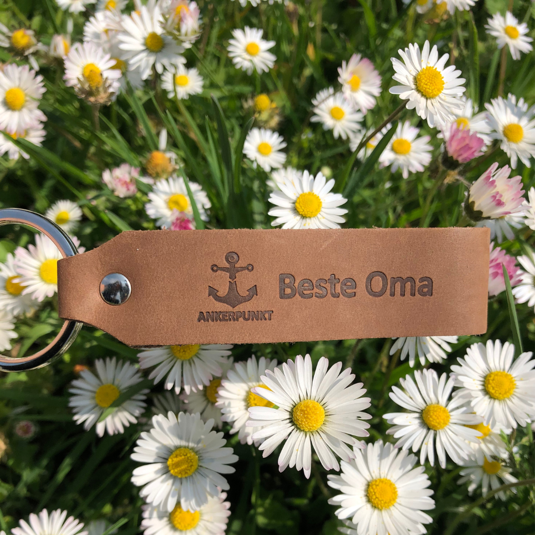 Beste Oma Schlüsselanhänger dunkelbraun liegt auf Blumen im Park